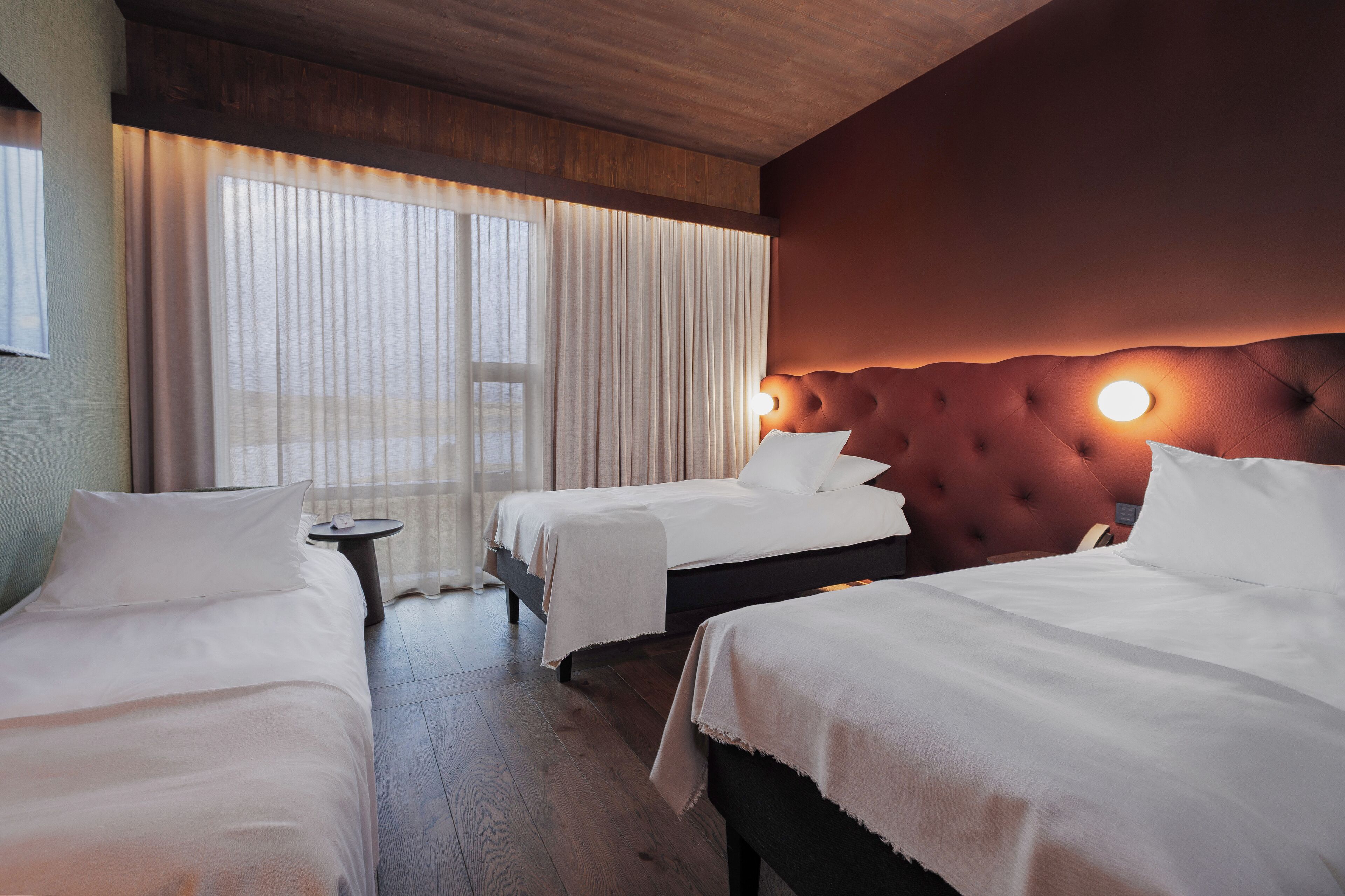 A hotel room with two beds, a small round table, and a large window with sheer curtains.
