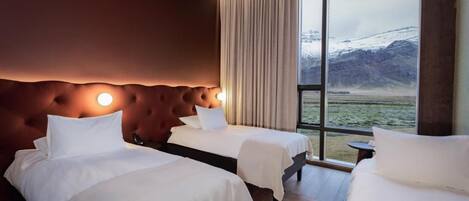 A hotel room with two beds, a large window with a view of mountains, and a wooden headboard.