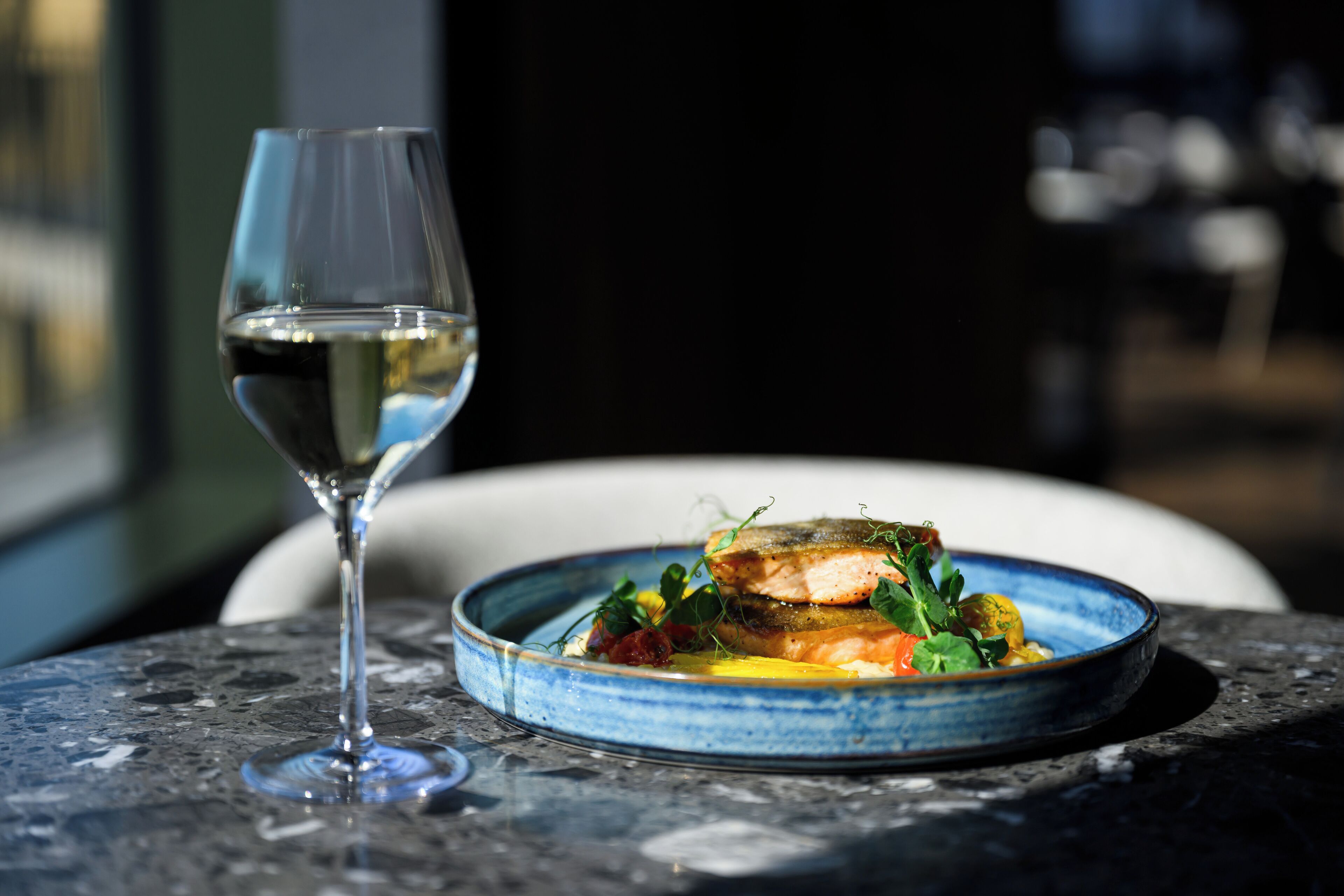 A plate of food with a glass of white wine on a table.