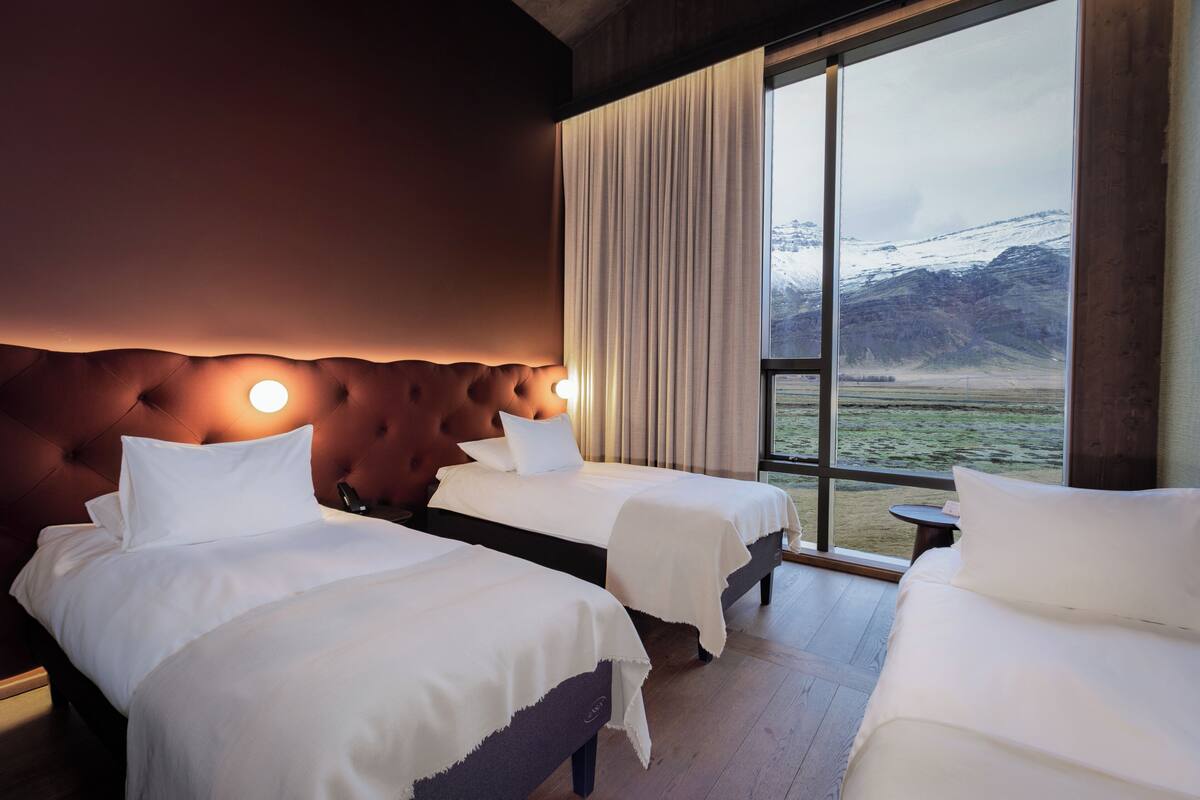 A hotel room with two beds, a large window with a view of mountains, and a wooden floor.