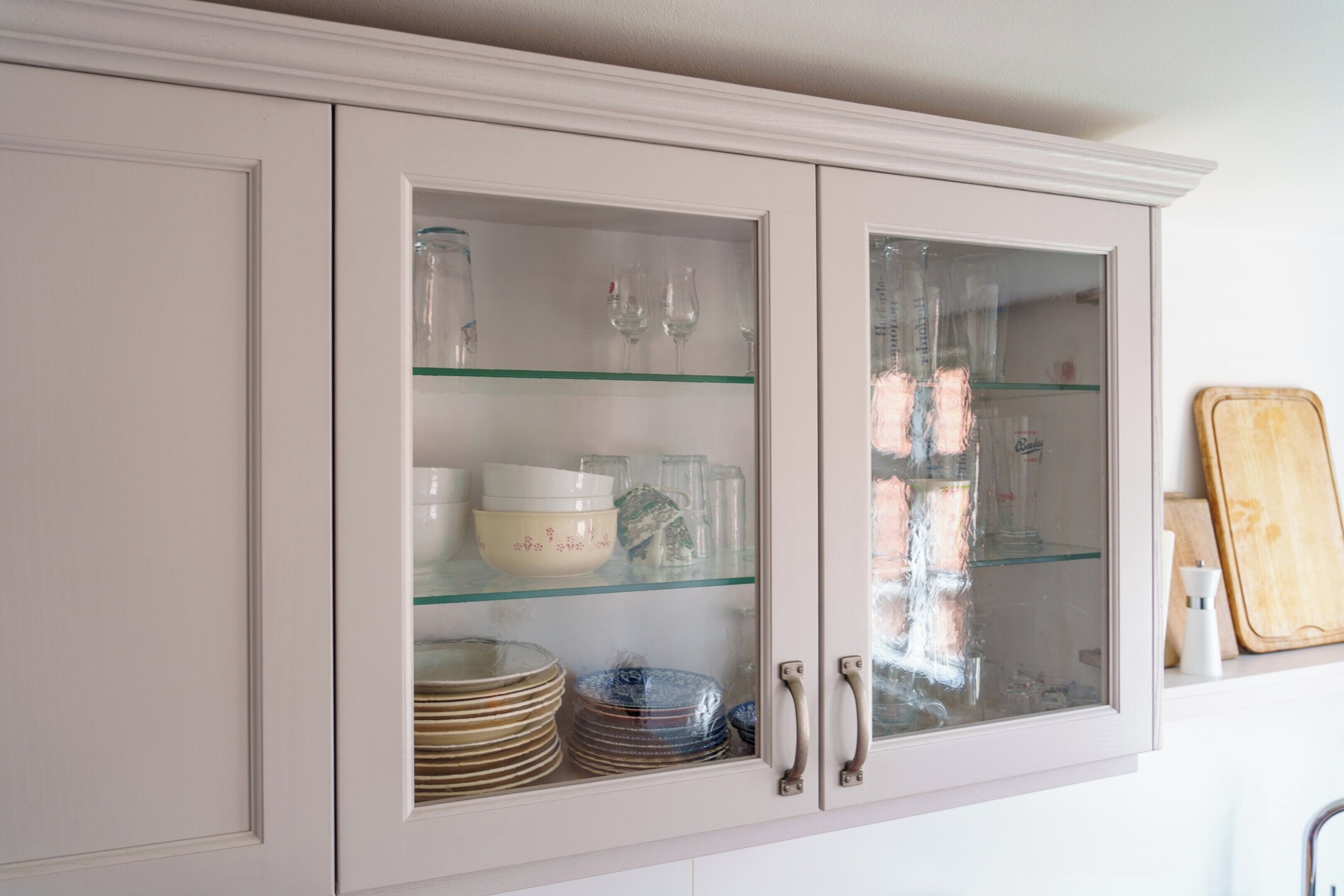 Un meuble de cuisine doté de portes en verre, dans lequel on peut voir des assiettes, des bols et des verres empilés.