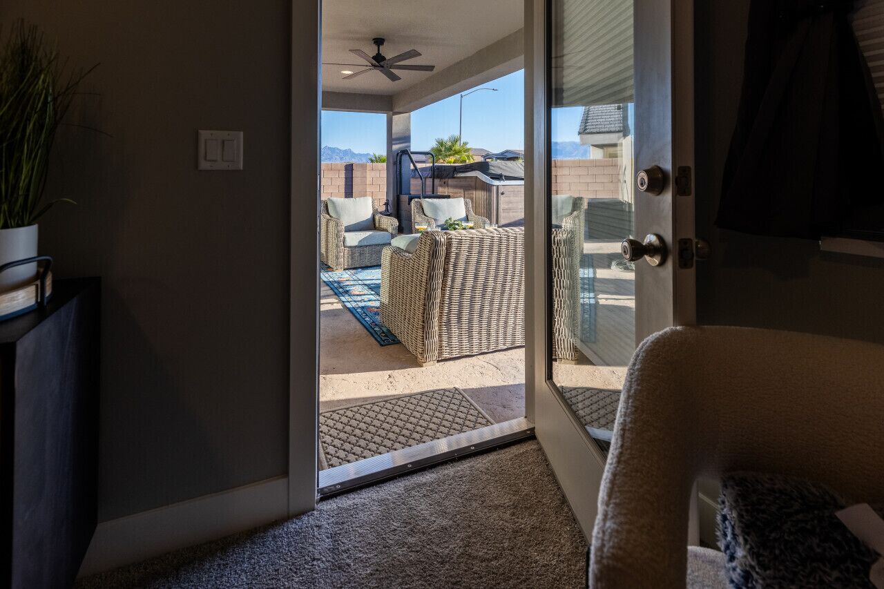 Un'apertura che dà su un patio esterno con mobili in vimini, una ventola a soffitto e vista sulle montagne.
