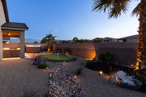 Un patio trasero ajardinado con jacuzzi, un área de estar techada y un jardín bien cuidado con rocas y plantas.