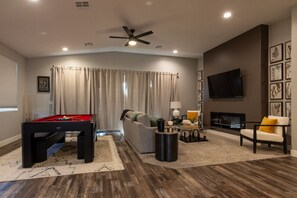 Una sala de estar moderna con mesa de billar, sofá, chimenea y televisor de pantalla plana montado en la pared.