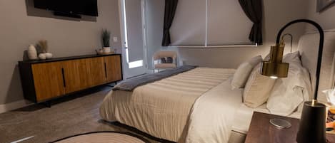 A bedroom with a bed, a TV, a wooden cabinet, a chair, and a window with curtains.