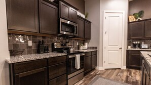 A kitchen with dark cabinetry, a stainless steel microwave, a stove, and a coffee maker. - Par-Tee Timers Paradise by J and Amy BL105619026 (Mesquite)