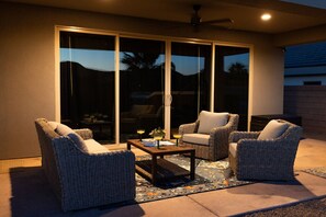 Un patio al aire libre con mobiliario de mimbre, una mesa de centro y vistas a través de grandes puertas corredizas de vidrio.