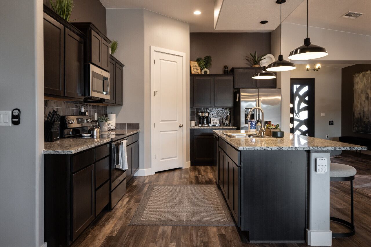 A modern kitchen with dark cabinetry, a central island, and pendant lighting.