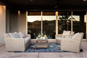 Un patio con mobiliario de mimbre, una mesa de centro y una alfombra estampada.
