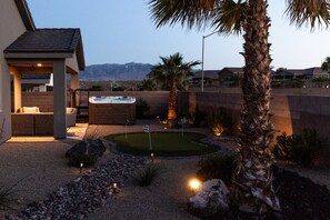 Un patio trasero con jacuzzi, una terraza con asientos y un césped bien cuidado.