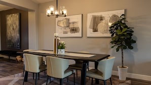 Een eetruimte met een rechthoekige tafel, vier stoelen, een kroonluchter en twee abstracte schilderijen aan de muur.