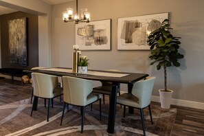 Un comedor con una mesa rectangular, cuatro sillas, una araña y dos cuadros abstractos en la pared.