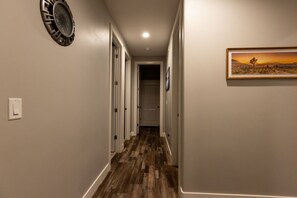 Un pasillo con suelo de madera, un reloj de pared y un cuadro enmarcado.