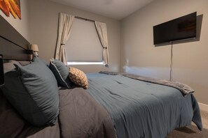 Ein Schlafzimmer mit einem Bett, einem Fernseher, einem Fenster mit Vorhängen und einer Lampe.
