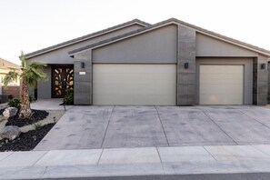A modern two-story house with a garage, a driveway, and a small garden with a palm tree. - Par-Tee Timers Paradise by J and Amy BL105619026 (Mesquite)