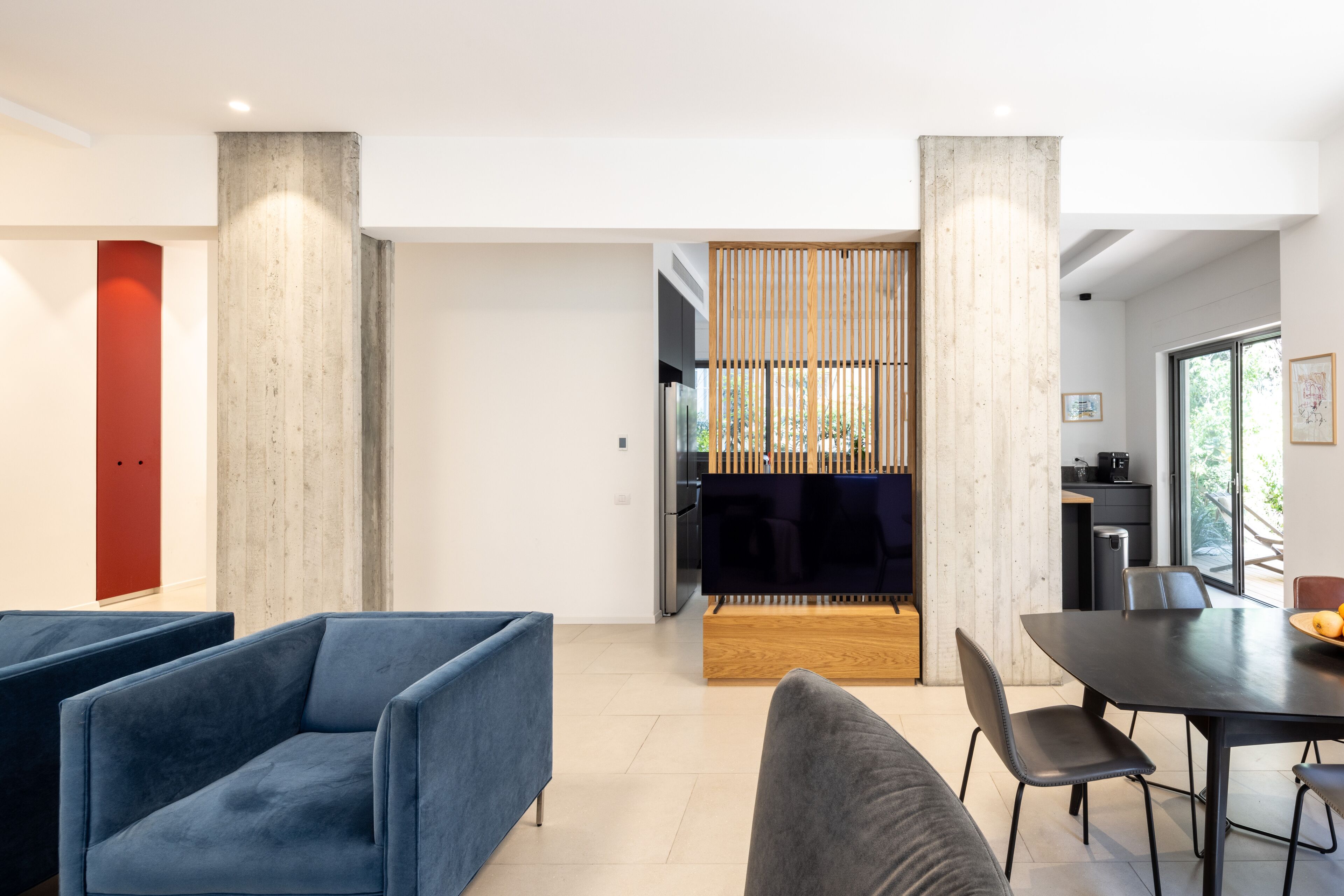 A modern living space with a dining area, a kitchen, and a red accent wall.