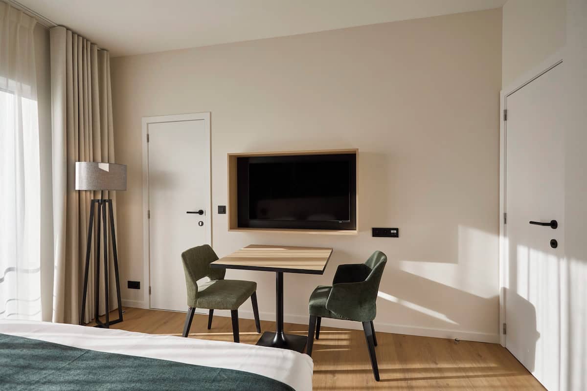 Une chambre d’hôtel comprenant un lit, un bureau avec deux chaises, un téléviseur fixé au mur et une lampe.