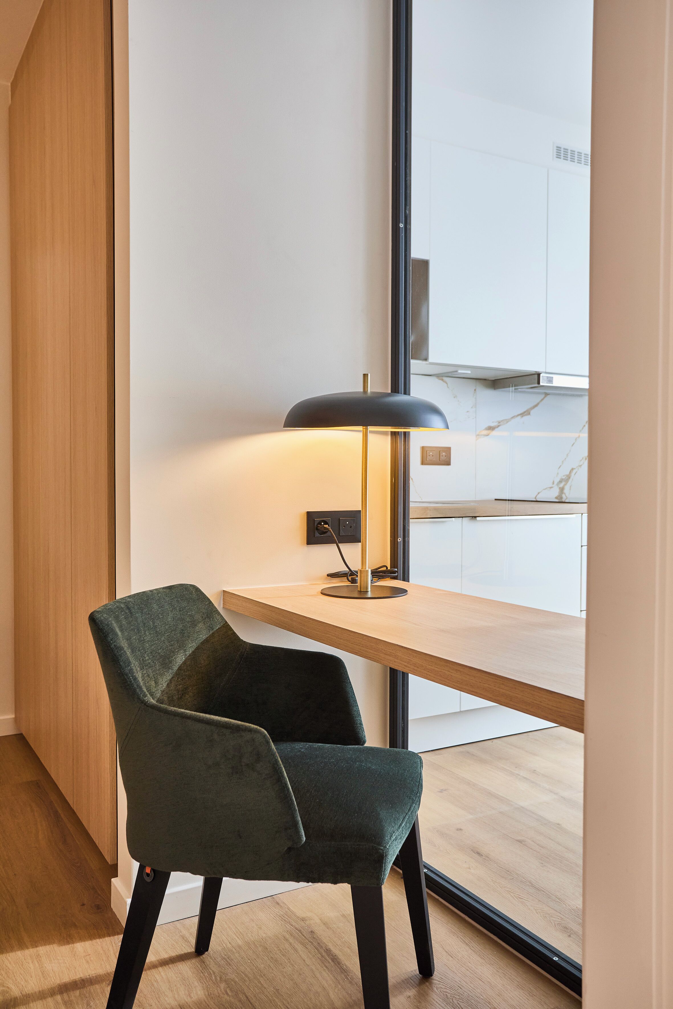 A modern kitchen with a wooden countertop, a black pendant lamp, and a green upholstered chair.