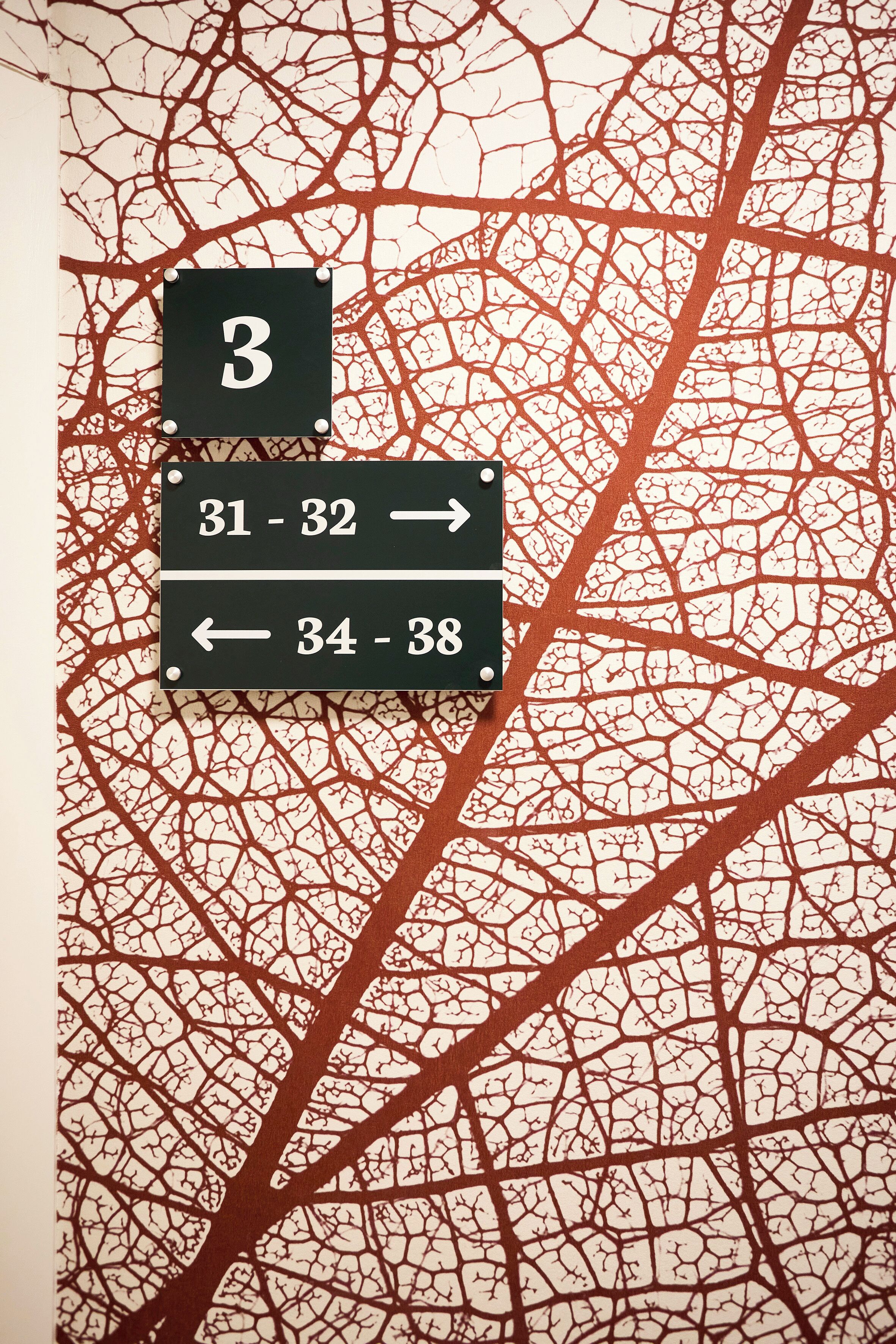 Eine Wand mit einem Schild mit der Nummer 3 und Pfeilen, die die Zimmernummern 31 bis 32 sowie 34 bis 38 anzeigen.