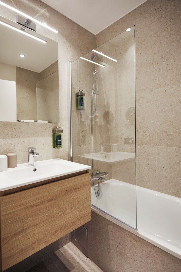 Un baño moderno con ducha de vidrio, tocador de madera y lavamanos blanco.