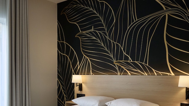 A hotel room with a large bed, a dark wall with a leaf pattern, a wooden headboard, and a nightstand with a lamp. - Georges Henri Aparthotel (Brussels)