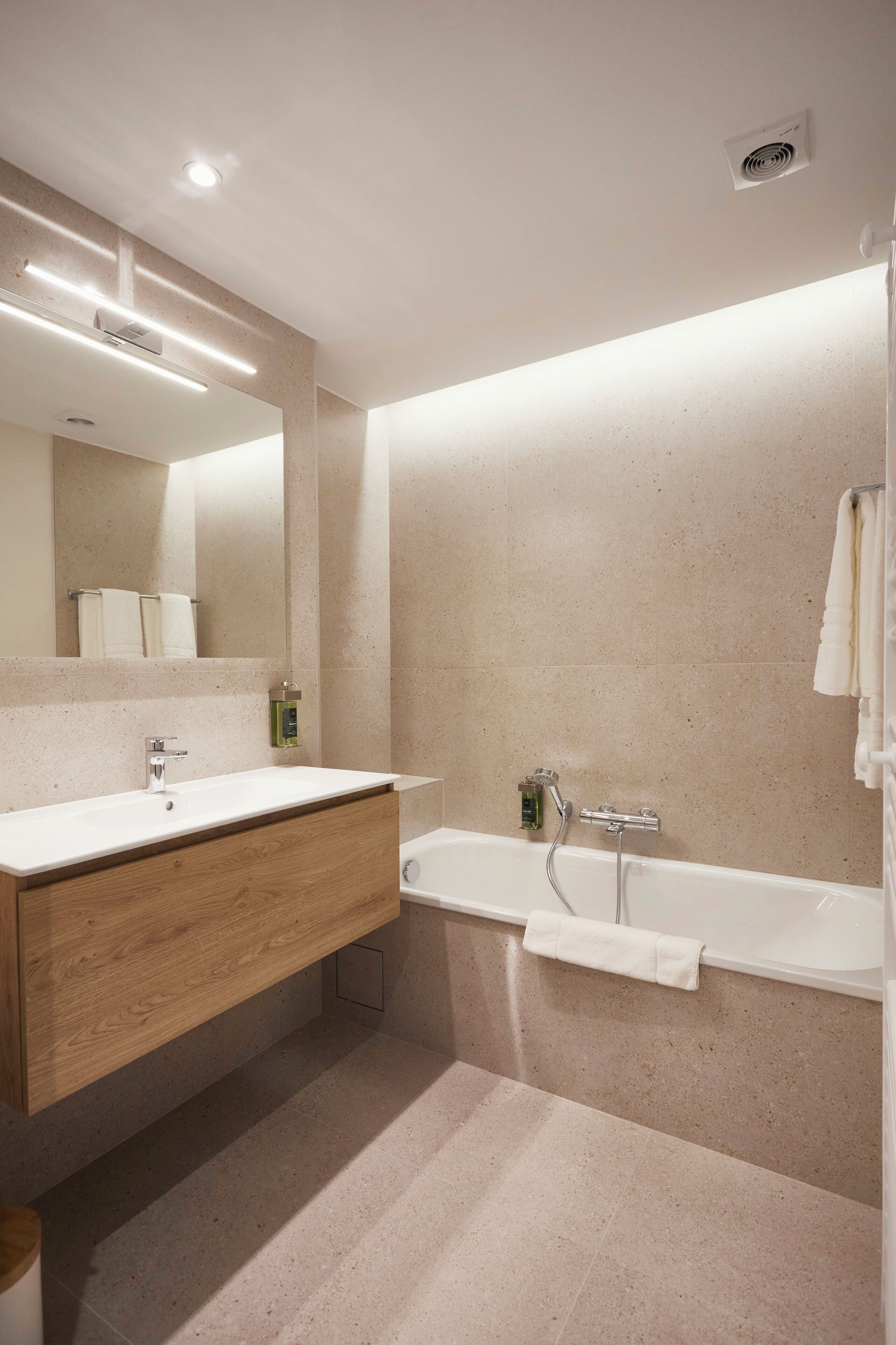 Een moderne badkamer met een houten wastafelmeubel, een vrijstaand bad en een grote spiegel.