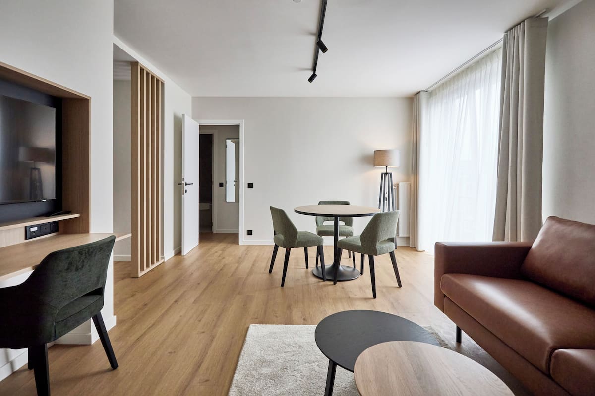Un salon moderne doté d’un téléviseur à écran plat, d’un canapé en cuir marron, d’une table de salle à manger ronde avec quatre chaises et d’un plancher en bois.