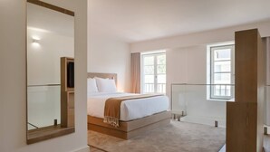 A modern hotel room with a large bed, a TV, and a large window providing natural light.