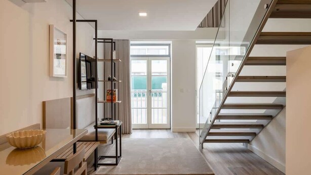A modern interior with a staircase, a dining area with a glass table, and a view through a glass door.