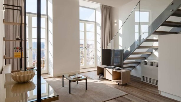 Una sala de estar moderna con una mesa de centro de vidrio, un televisor de pantalla plana y una escalera con barandilla de cristal.