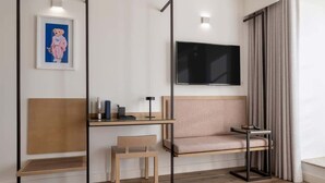 Une chambre d’hôtel moderne avec un bureau en bois, un canapé confortable, un téléviseur fixé au mur et une fenêtre avec des rideaux.