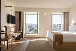 A hotel room with a large bed, a desk, a TV, and a view of the city through two windows. - Fervença Boutique Palace 6 by HostWise (Vila Nova de Gaia)