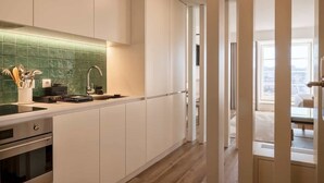A modern kitchen with white cabinetry, a green tiled backsplash, and a view of the city through a large window.