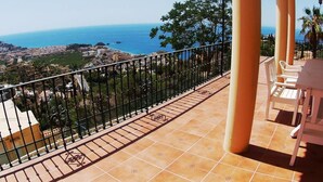 Eine Terrasse mit Blick auf das Meer und die Stadtlandschaft, mit Fliesenboden und Metallgeländer.