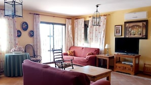 Ein Wohnzimmer mit Sofa, Sessel, Couchtisch, TV-Schrank und einem Tisch mit Lampe.