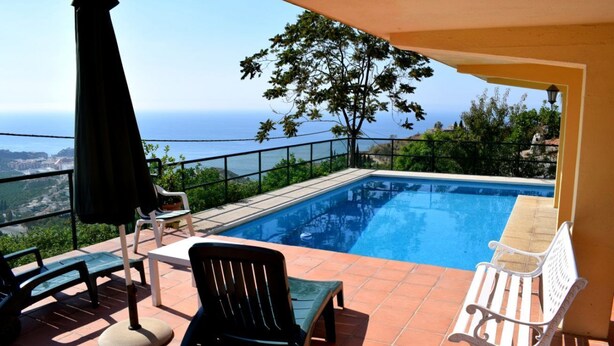 Ein Poolbereich mit Blick auf das Meer, Gartenmöbel und ein Baum.