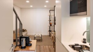 A modern kitchen with a built-in microwave, a coffee machine, and a sink. There is a wooden table and a ladder in the background. - Fervença Boutique Palace 4 by HostWise (Vila Nova de Gaia)