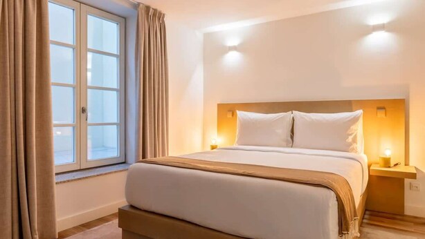 A hotel room with a large bed, two bedside lamps, a window with curtains, and a nightstand. - Fervença Boutique Palace 4 by HostWise (Vila Nova de Gaia)