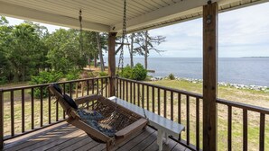 Une terrasse en bois avec une chaise suspendue et un banc, d’où l’on peut admirer un plan d’eau.