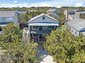 A two-story house with a balcony, surrounded by trees and other houses.