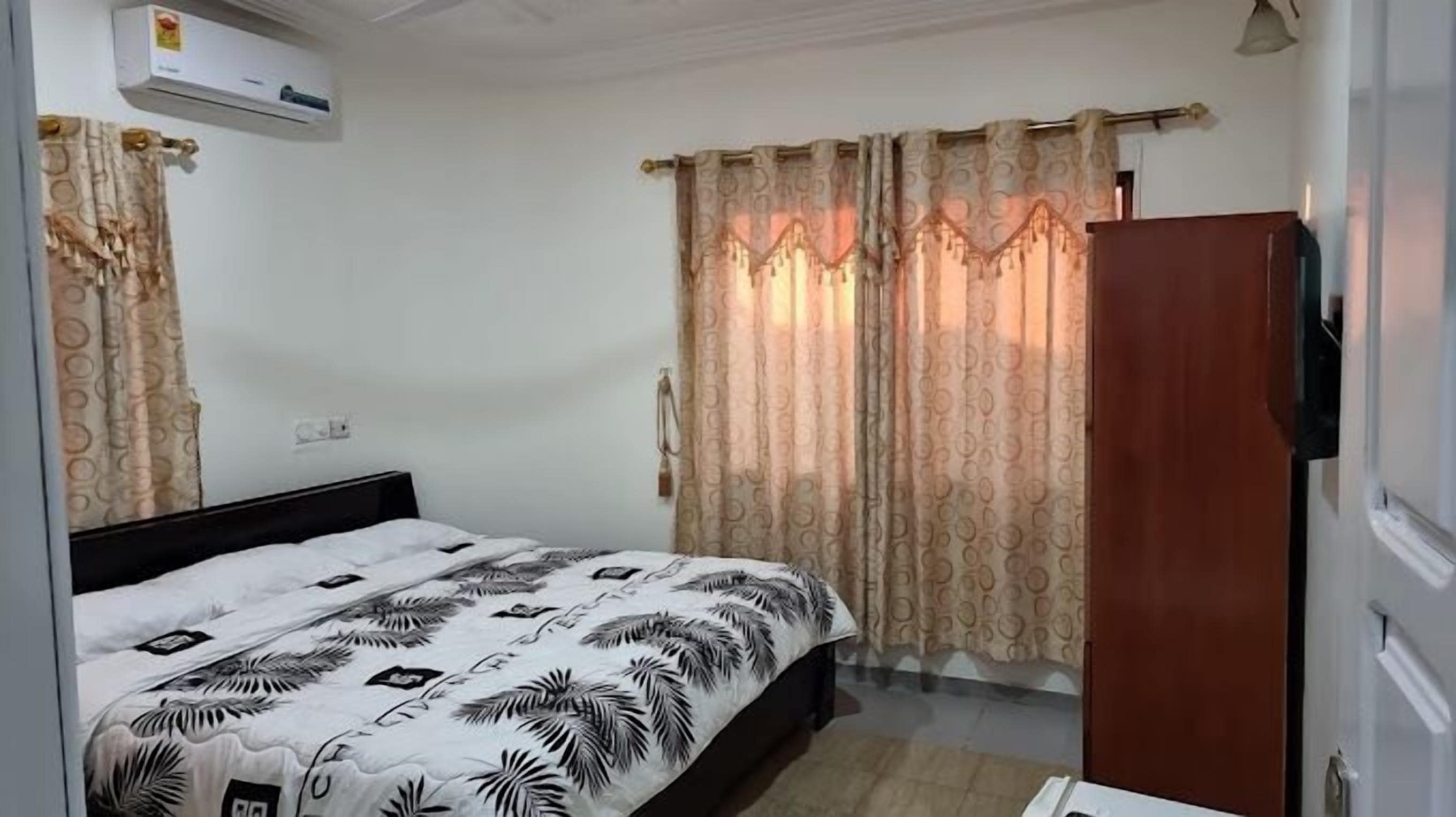 Ein Schlafzimmer mit Bett, Vorhängen, Kleiderschrank und Klimaanlage.