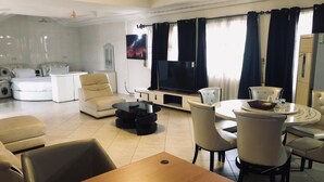Ein modernes Wohnzimmer mit einer Sofagarnitur, einem Esstisch mit Stühlen, einem Flachbildfernseher und einem Deckenventilator.