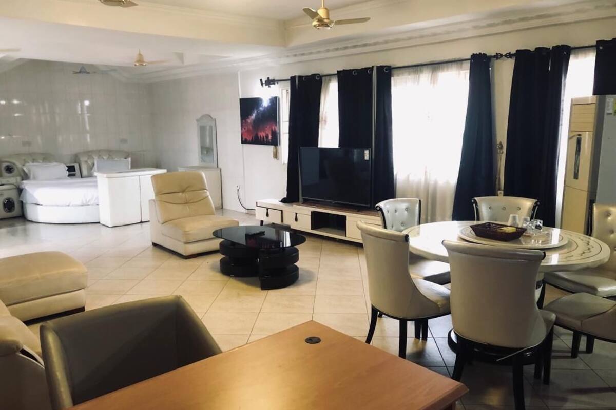 A modern living room with a sofa set, a dining table with chairs, a flat-screen TV, and a ceiling fan.
