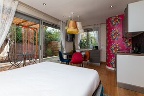A bedroom with a bed, a desk, and a chair, a balcony with a table and chairs, and a kitchen area.