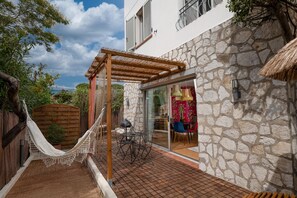 A stone building with a wooden pergola, a hammock, and a dining area with chairs and a table.