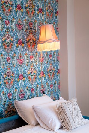 A room with a patterned wallpaper, a bed with white pillows, and a hanging lamp.