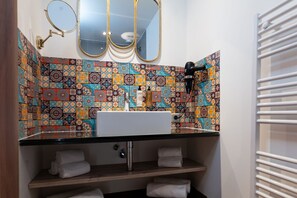 A bathroom with a sink, three mirrors, a towel rack, and a patterned tile backsplash.