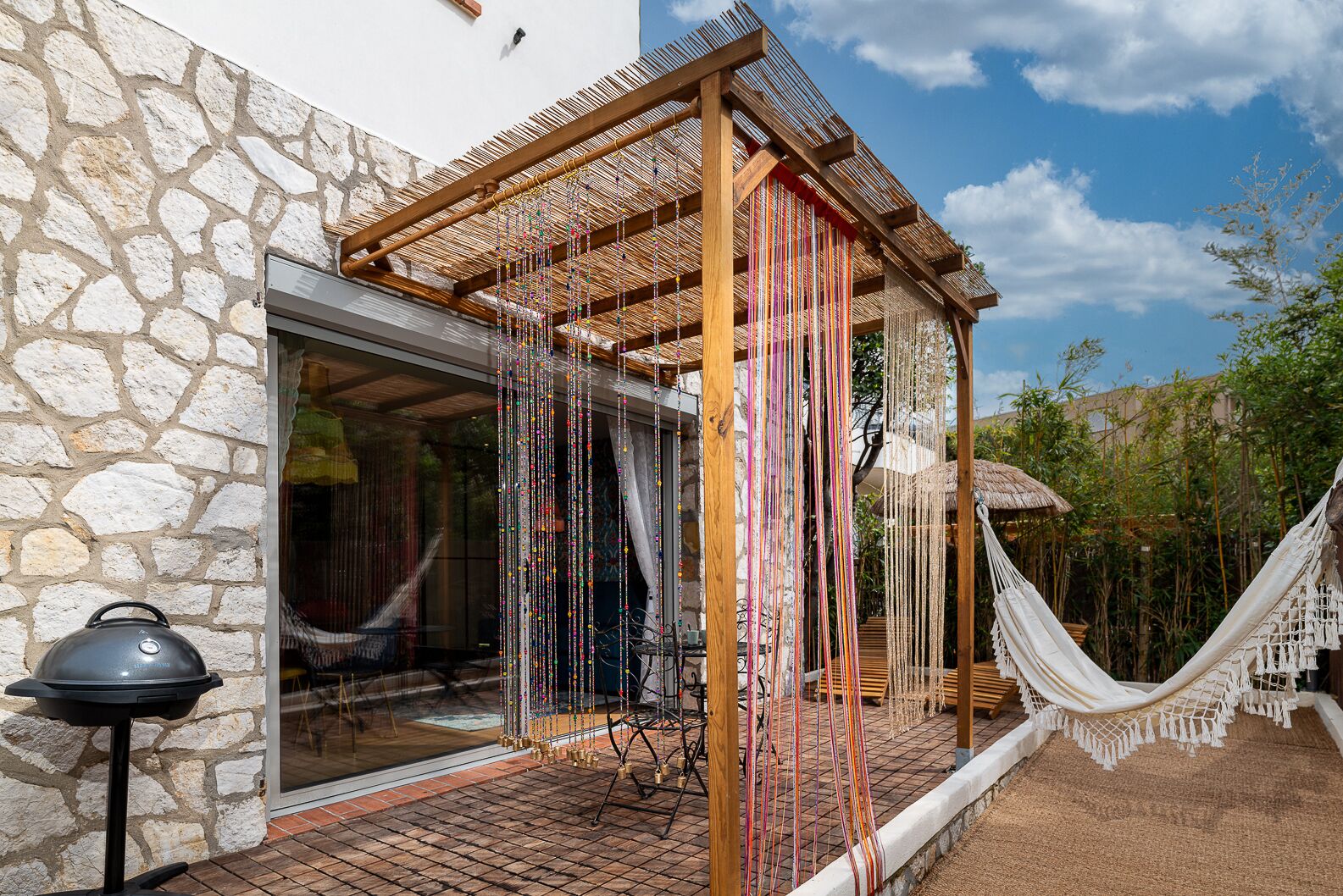 Un edificio in pietra con una pergola in legno, un'amaca e un barbecue all'esterno.
