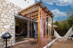 A stone building with a wooden pergola, a hammock, and a grill outside.