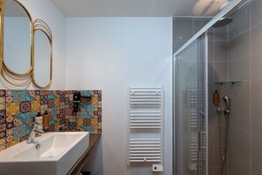 A bathroom with a white sink, a mirror, a colorful tiled backsplash, a white towel rack, and a glass-enclosed shower area.